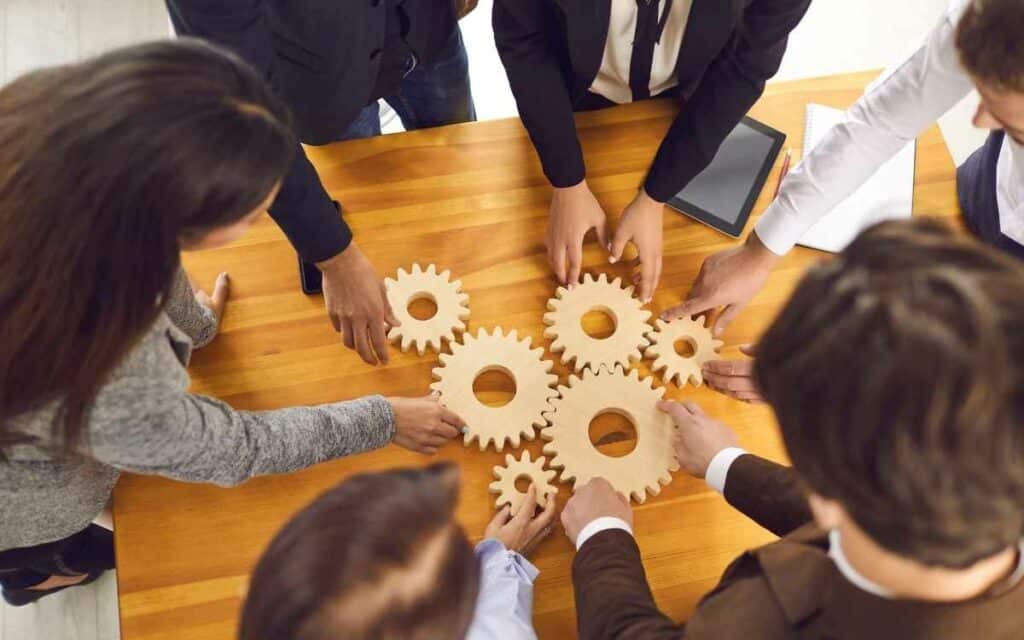 Vemos una imagen de cómo administrar un negocio con un equipo de personas uniendo unas piezas de engranaje, trabajndo en equipo.