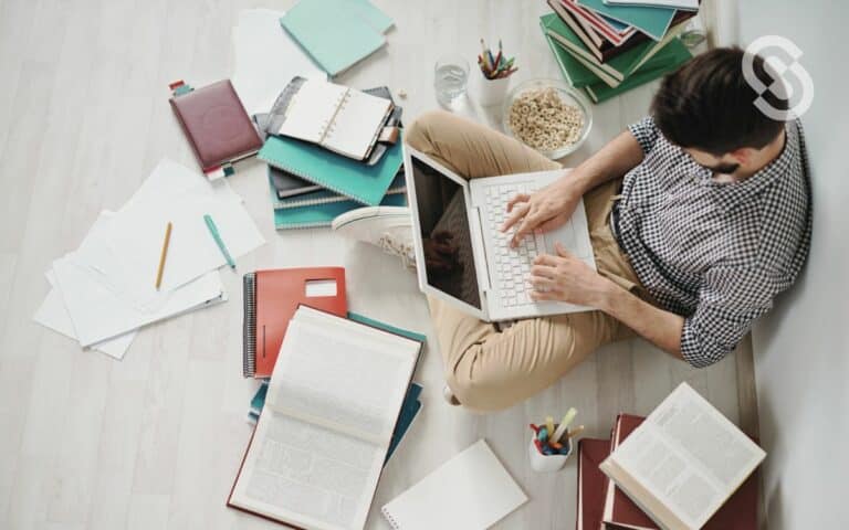 Vemos una imagen de una persona trabajando sobre técnicas de recolección de datos cualitativos con una computadora y muchos libros