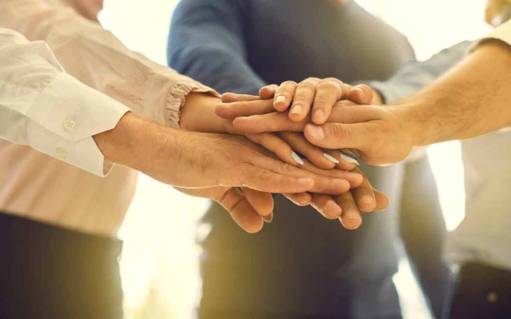 Vemos una imagen de un equipo de trabajo llegando a un acuerdo al colocar las manos al centro, como resultado de un buen manejo de conflictos.