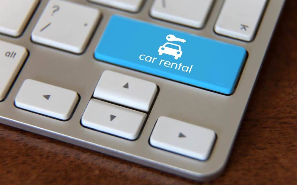 Teclado con una tecla azul que tiene el icono de un auto y la etiqueta "car rental", simbolizando la digitalización de empresas de alquiler de autos mediante el uso de tecnologías avanzadas.
