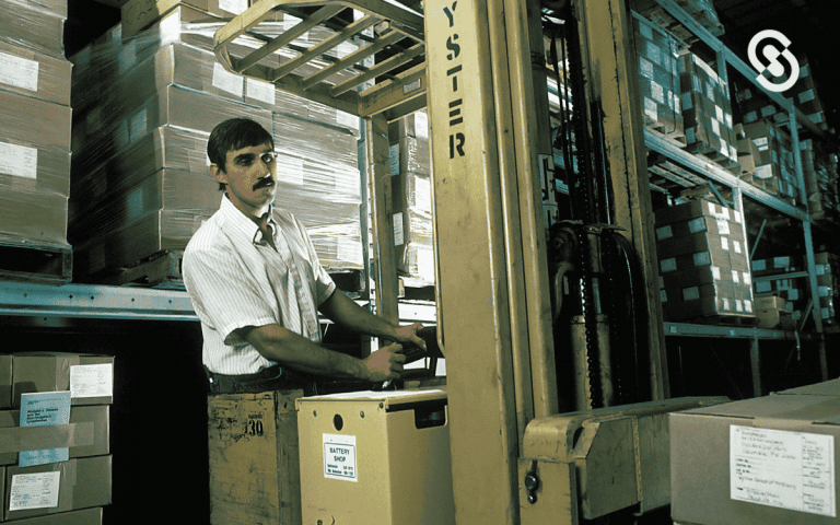 Un trabajador operando un montacargas en un almacén lleno de cajas apiladas en estanterías, simbolizando procesos logísticos y de planificación en el contexto de las diferencias entre MRP y ERP.