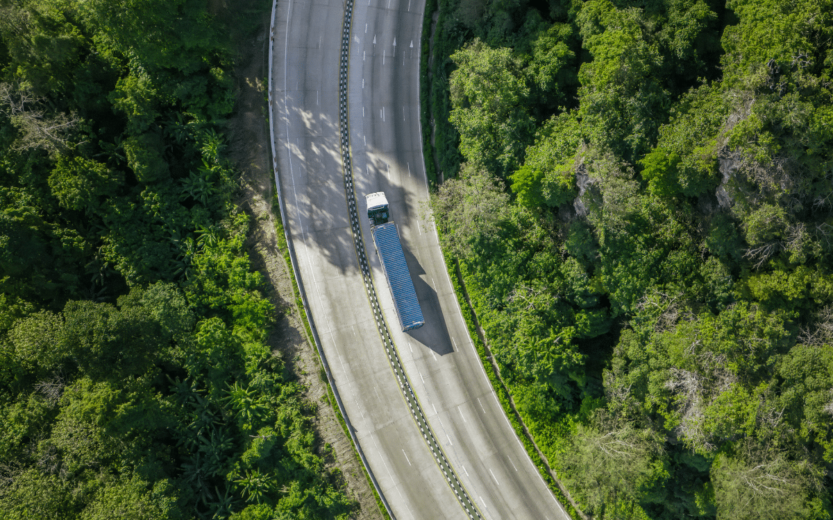 Vemos un camión de carga atravesando una ruta con árboles alrededor, en relación con la logística sostenible que promueve Drivin.